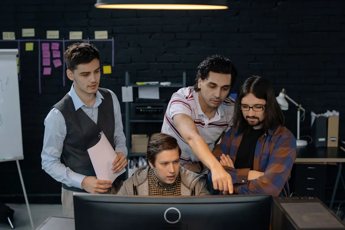 Four engineers gathered around one monitor, reviewing work together
